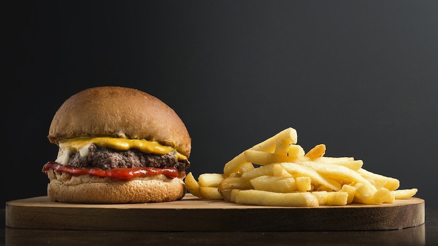 A hamburger and chips on a wooden board.