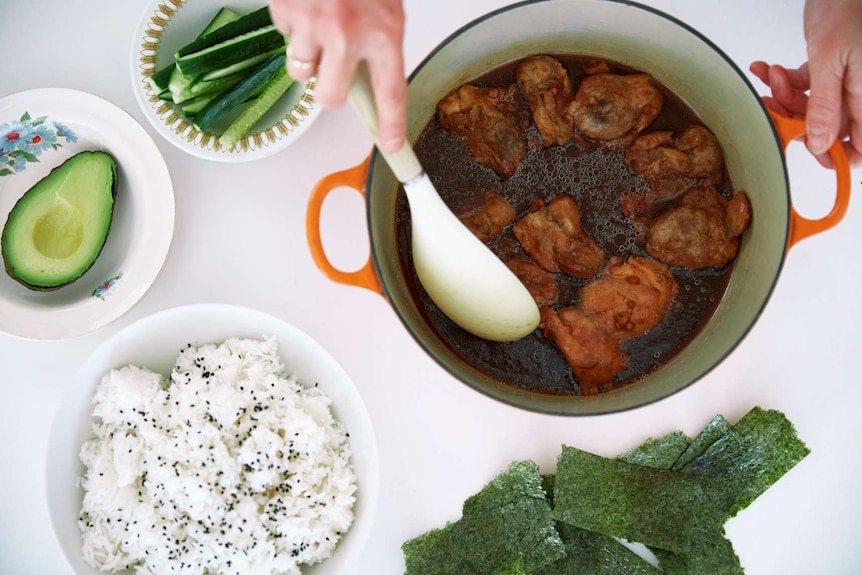 Baked teriyaki chicken in a pot, about to be served over rice with avocado and cucumber strips, family dinner.