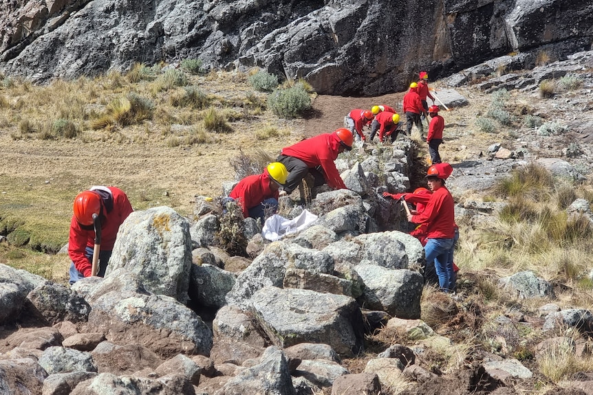 People in red jackets and helmets work arranging rocks in a makeshift dam. 
