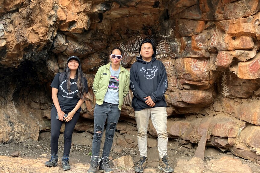 three First Nations people from Canada standing in front of Indigenous rock art in Australia.