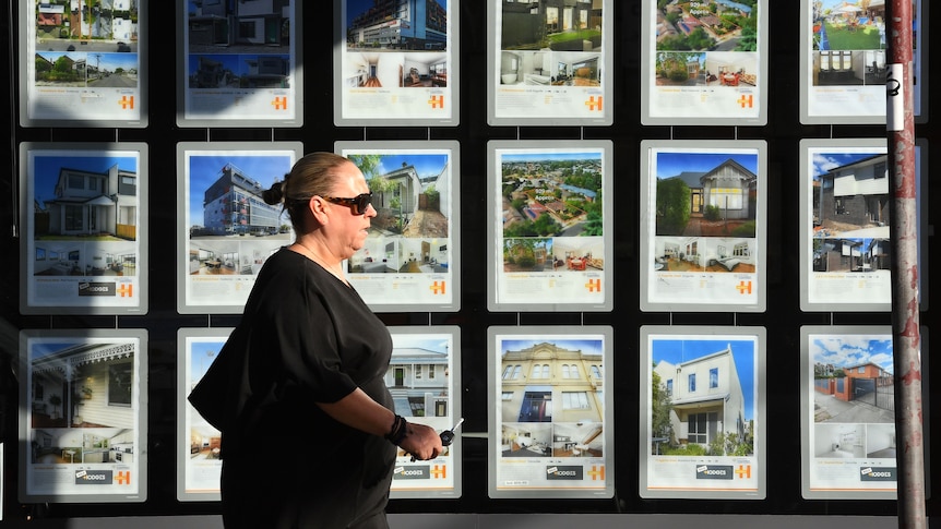 A woman walks past a real estate agent's window advertising houses for sale