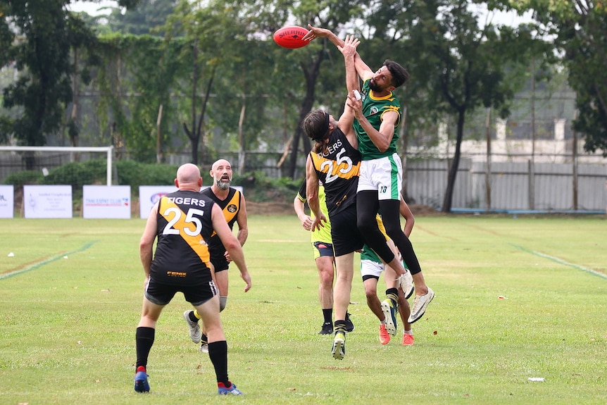 A footballer in a green singlet wins a hitout, surrounded by opposition players