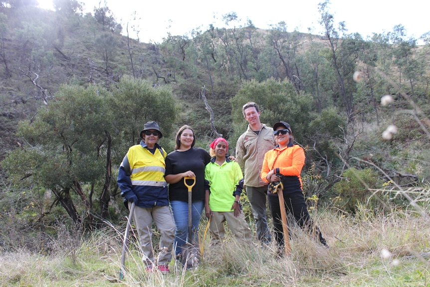 Image of four women in work clothes and a man in khaki in a natural bush environment with shovels