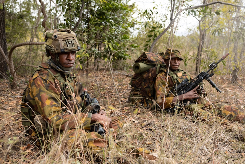 Two troops from PNG Defence Force hold weapons in the bush.