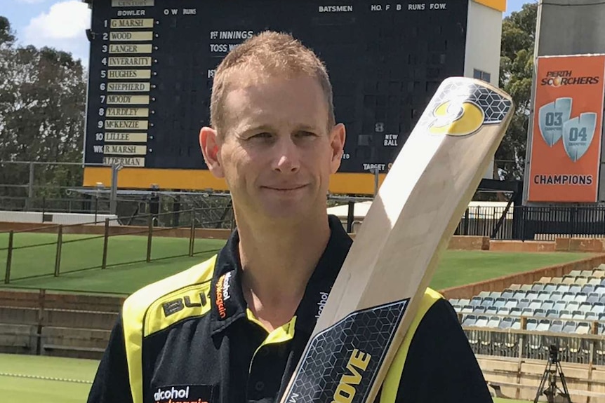 Adam Voges stands in front of the WACA Ground cricket scoreboard holding a bat against his shoulder.