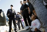 A photo from ground level shows children sitting on the ground surrounded by border protection authorities.