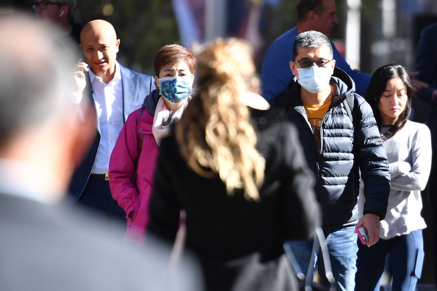 A group of people walk on a busy street, some wearing masks and some without.