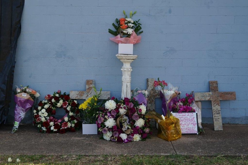 Flowers and crosses lined up along a wall.