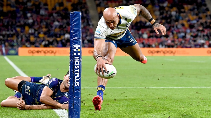 A Parramatta NRL player in mid-air as prepares to ground the ball with his right hand for a try.