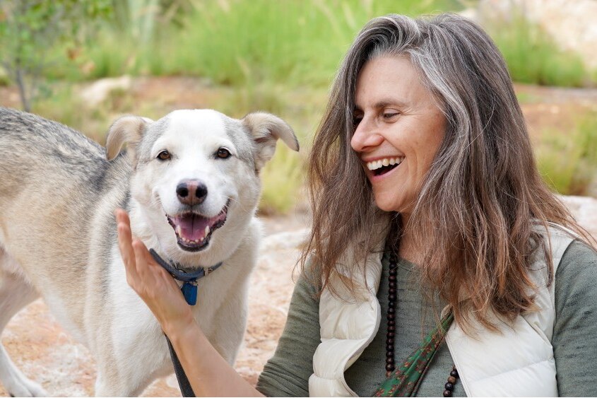 A woman smiles at her dog, which is looking at the camera.