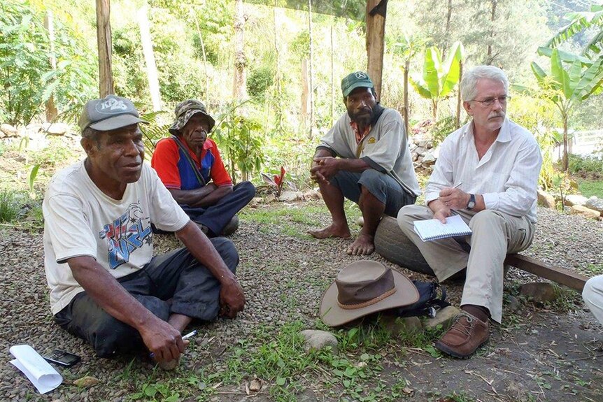 White man sits with native people of PNG