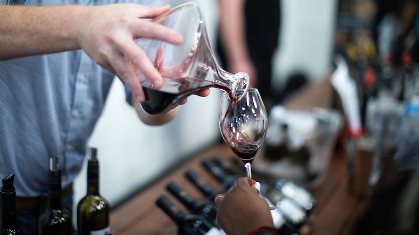 A hand is pouring red wine from a decanter into a wine glass being held by another person