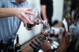 A hand is pouring red wine from a decanter into a wine glass being held by another person