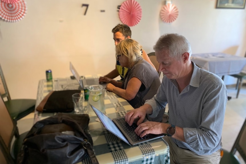 Journalists sit at a table typing on their computers.