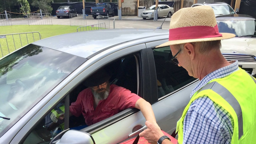 Man puts his ballot paper into a box that a voter official is holding near his car window