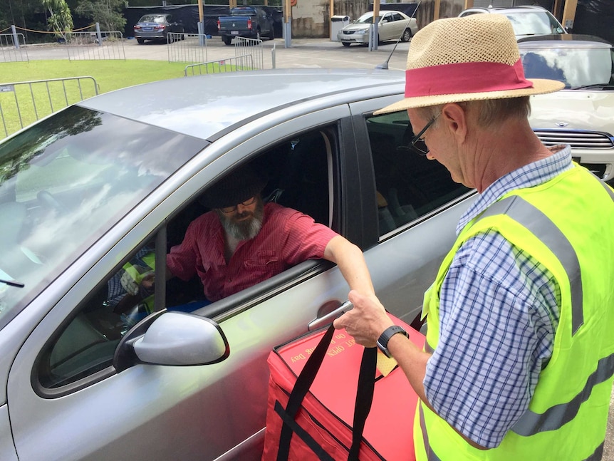 Man puts his ballot paper into a box that a voter official is holding near his car window