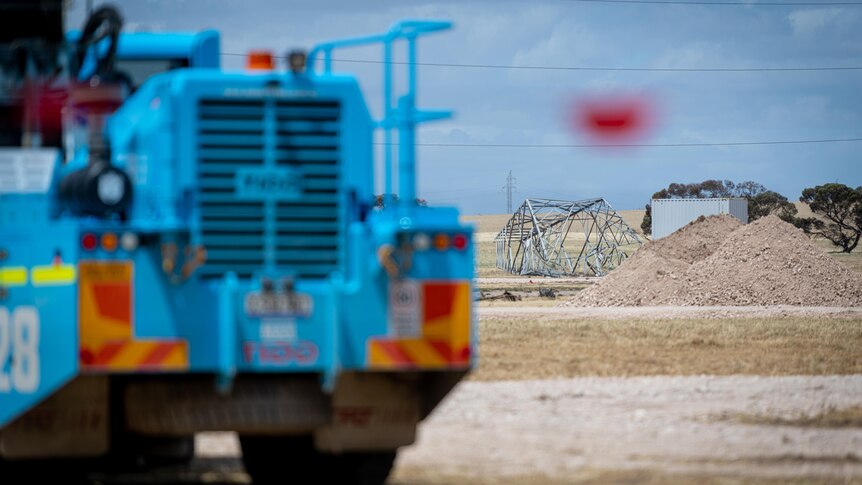 A blue truck in the foreground while in the background a transmission tower lays on the ground