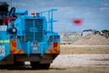 A blue truck in the foreground while in the background a transmission tower lays on the ground