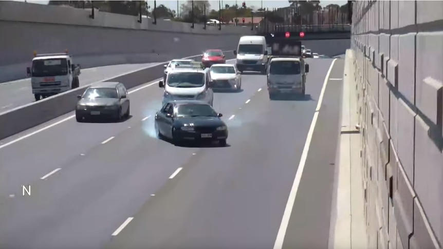 A car crossing lanes on a busy highway with smoke billowing from behind.