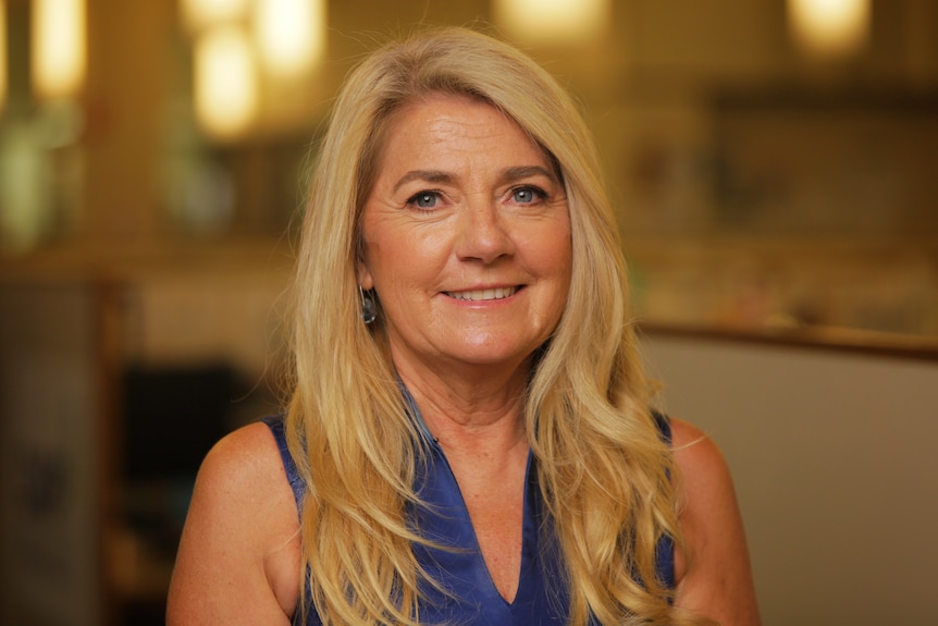 Woman with long blonde hair wearing a blue top. 