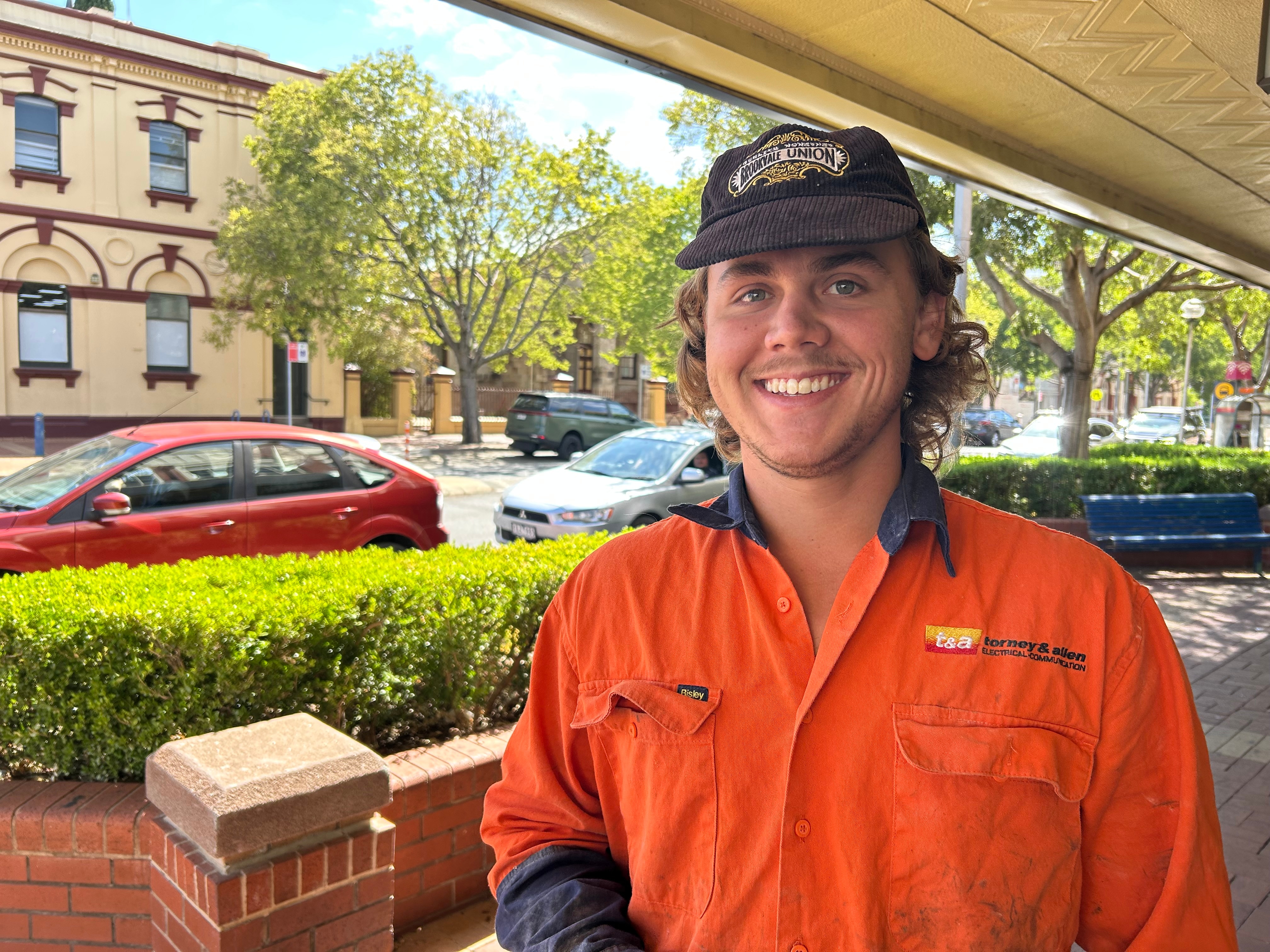 Un joven con un mono de alta visibilidad y una gorra marrón. 