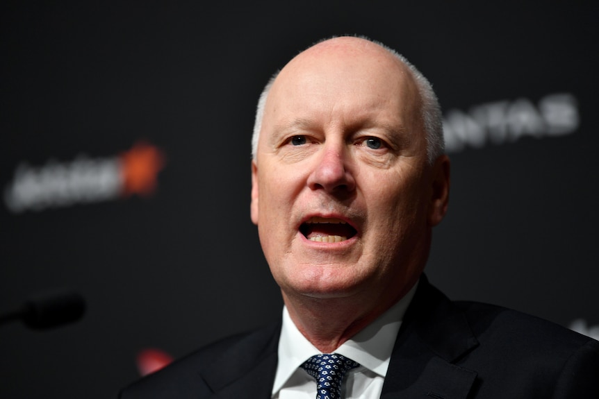 A man with glasses and a navy blue suit and tie stands behind a lecturn at a business conference