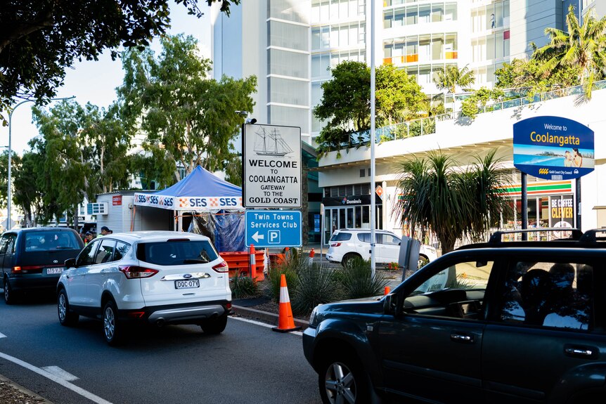 A line of cars on a road next to a makeshift tent. Signs say "Welcome to Coolangatta".