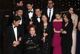 Cast and crew of Parasite in black tie on the Oscars stage accepting their award.