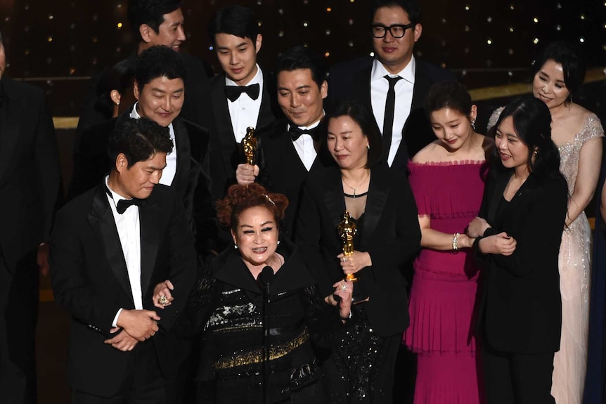 Cast and crew of Parasite in black tie on the Oscars stage accepting their award.