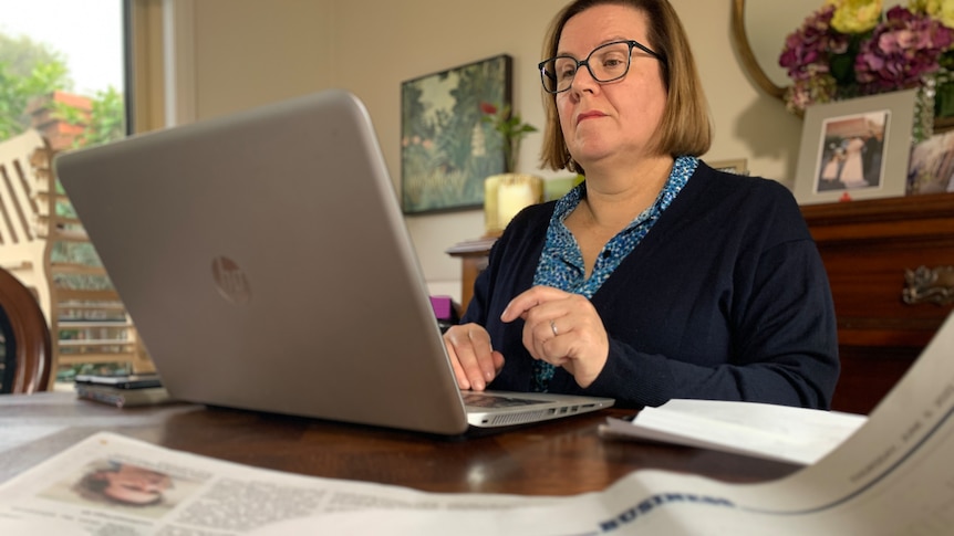 Rosemary using her laptop, with a newspaper article about green energy open on her table.