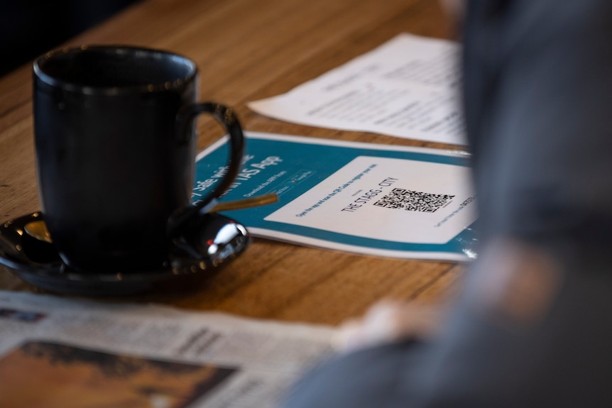 QR check in signage on a cafe table with cup nearby.