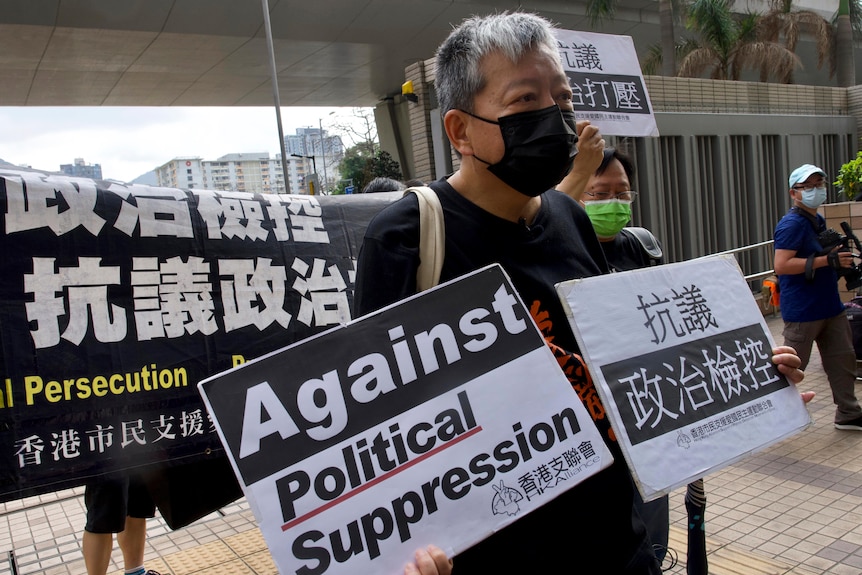 A man wearing black and a black mask stands holding signs with Chinese script