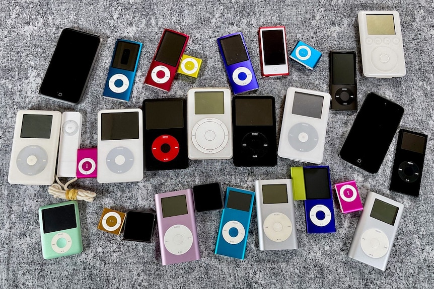 A collection of various models of Apple iPod from throughout the years, lying on a grey surface
