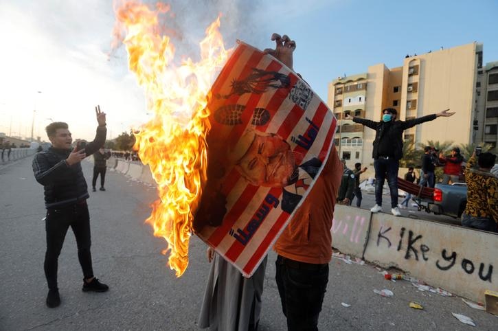 A protester holds a sign with Donald Trump's face while it's burning outside the embassy.
