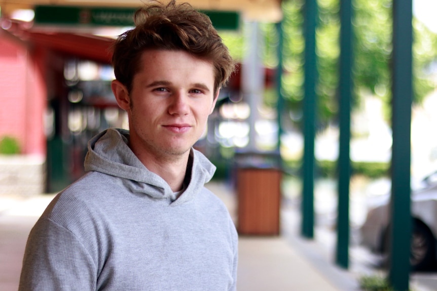 A portrait of a 19-year-old man in a grey hooded sweatshirt, standing outdoors