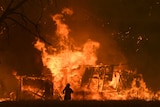 fire engulfs a structure as a man watches on