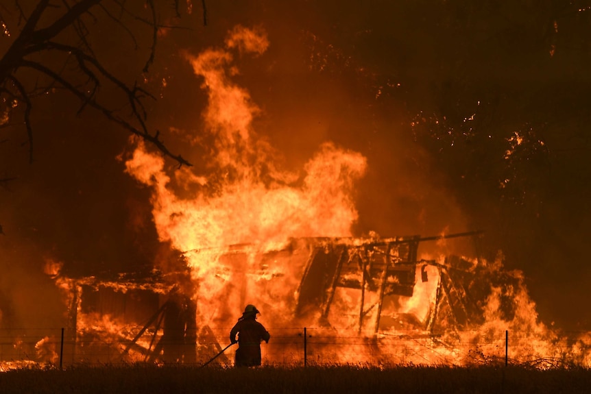 fire engulfs a structure as a man watches on