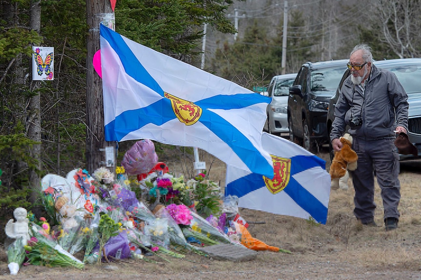 A older man pays his respects placing a teddy bear at a roadside memorial in Portapique.