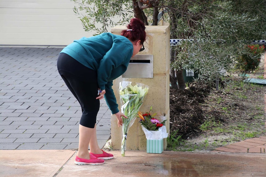 A woman bends down to lay a bunch of flowers on the ground under a letterbox outside a house.