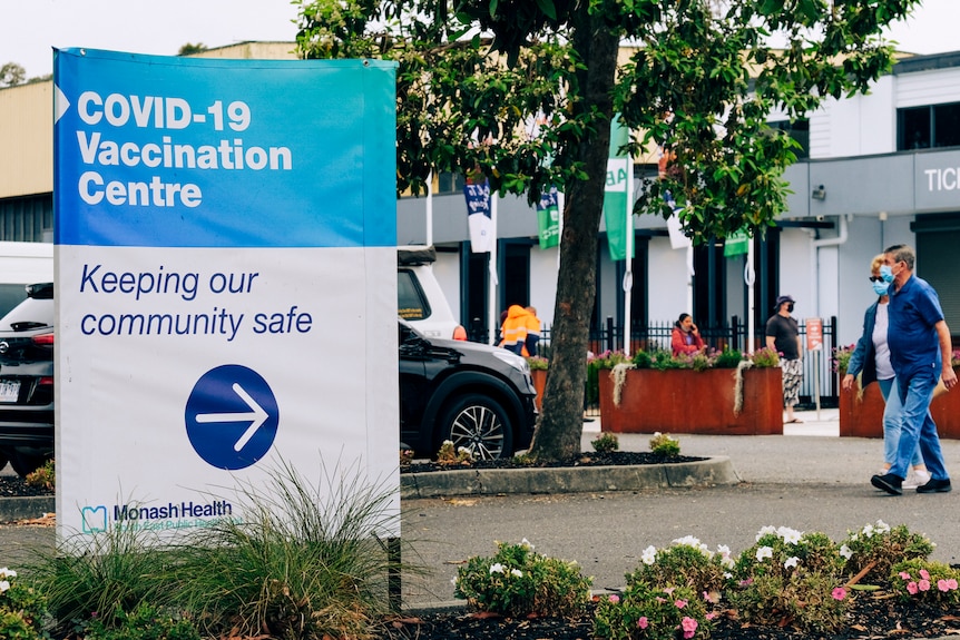 A sign reads 'COVID-19 Vaccination Centre: Keeping our community safe' as a masked couple walk by.