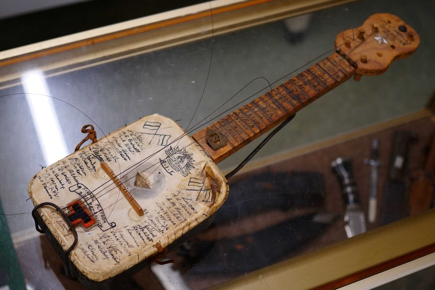 A wooden stringed instrument (banjo) inscribed with handwritten words.