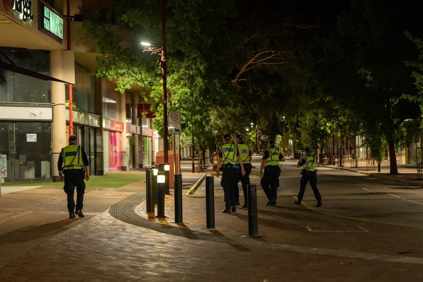 Police walk down an empty street at night lit up by street lights 