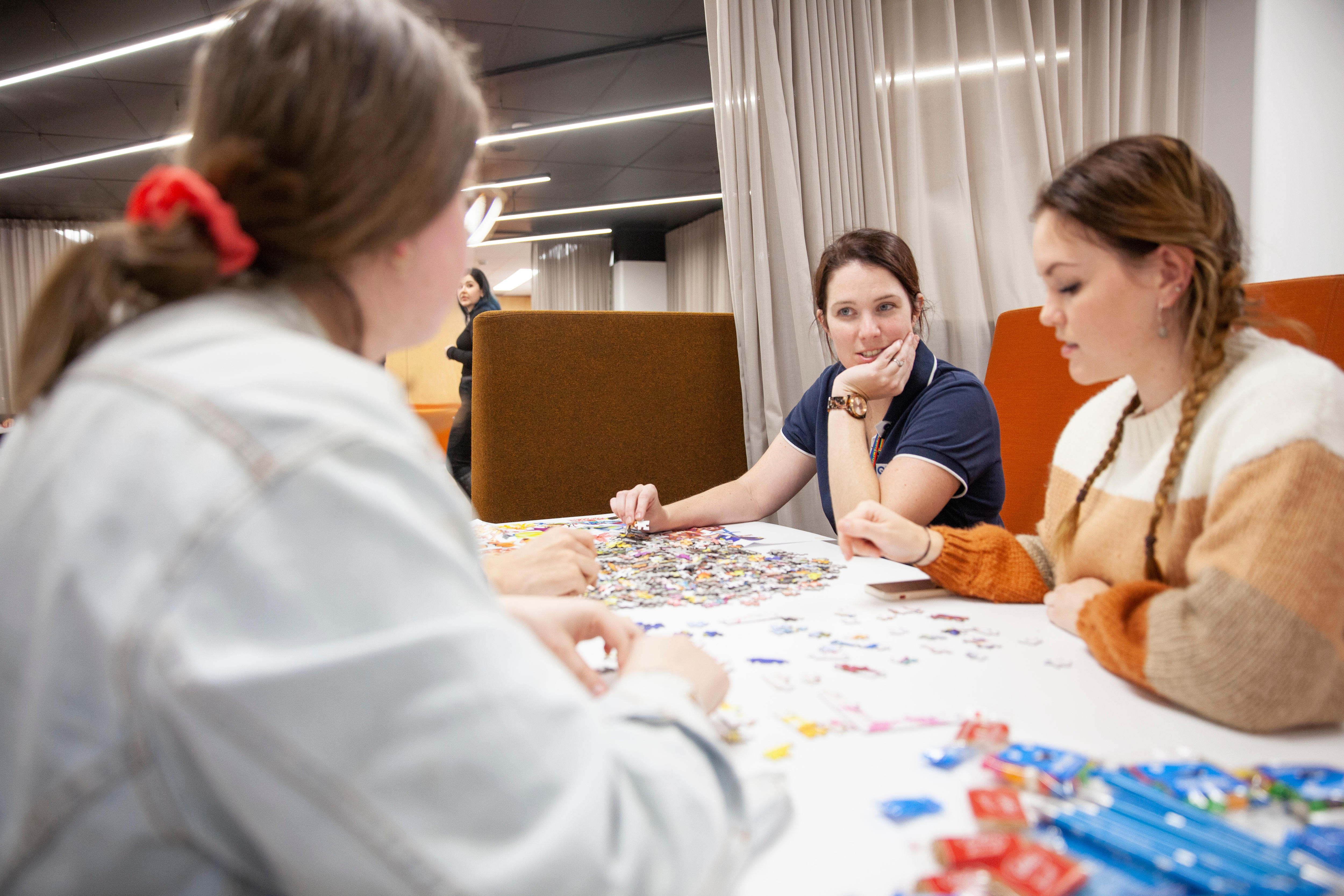 A woman talks to two students about a half-finished puzzle.