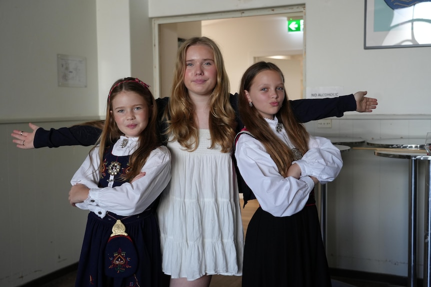 Three girls in traditional Norwegian dress pose for a photo.