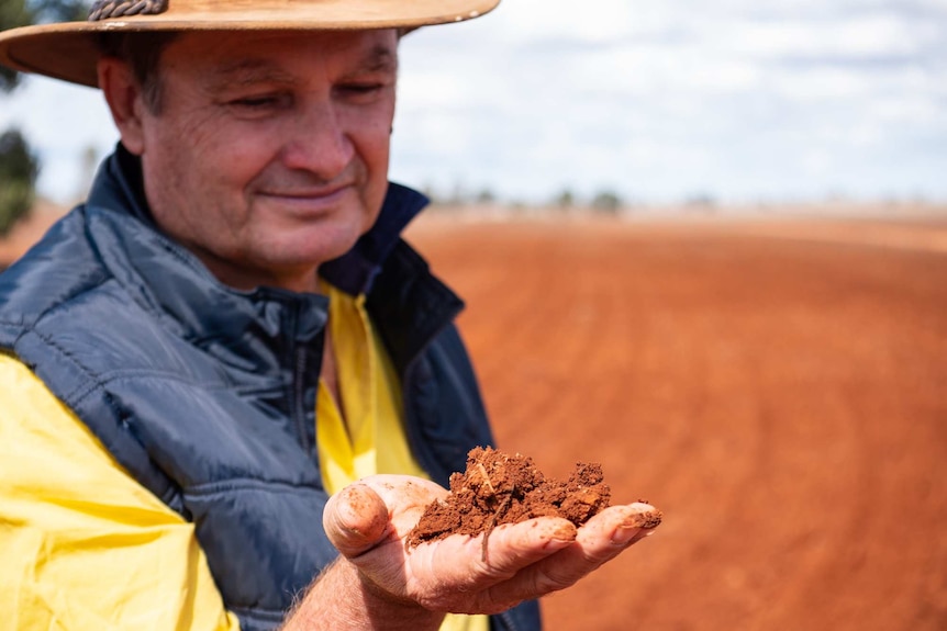 A man in a hat picks up a handful of soil.