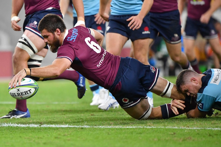 A Queensland Reds Super Rugby player dives over the goal line as he prepares to ground the ball with his left hand.