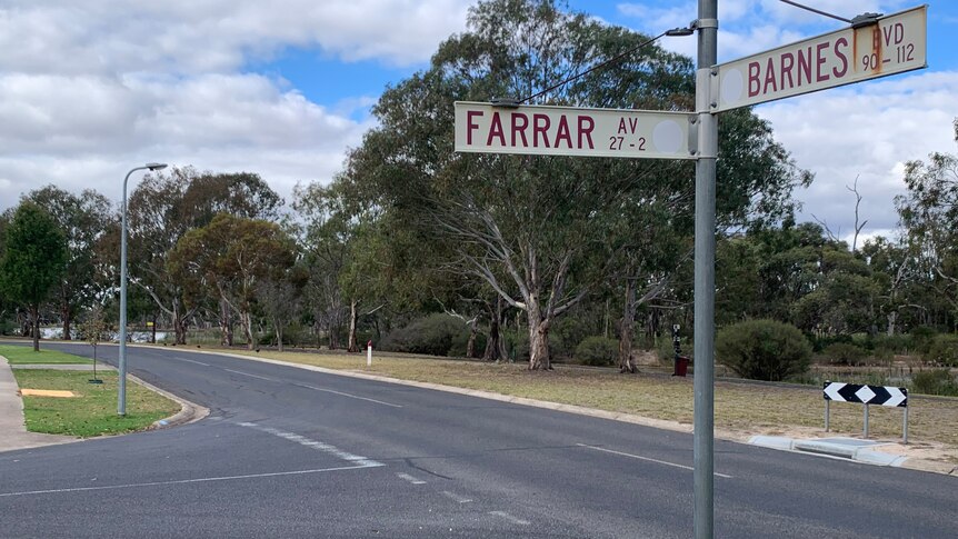 A street sign with red lettering stands in foreground with street and bush track behind