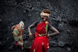 A middle-aged Indian female in traditional garb has hands on hips as she smiles in front of coal mine