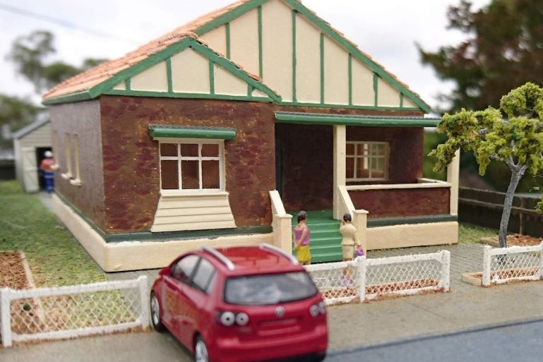 A photo of miniature people standing outside a miniature house.