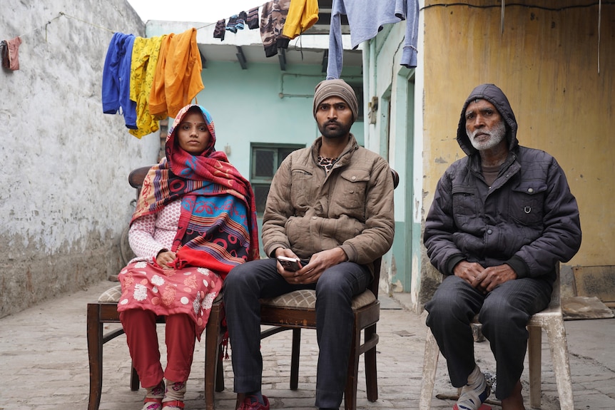 A close up of three people sitting on chair outside their home.